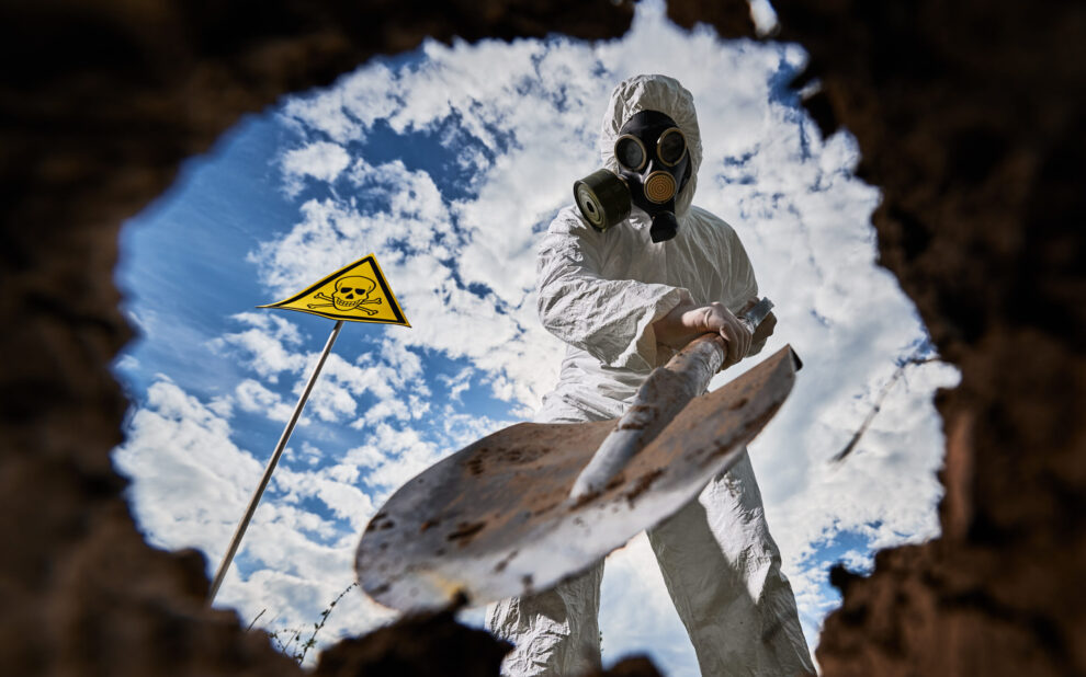Ecologist digging pit by shovel and planting tree in polluted area.